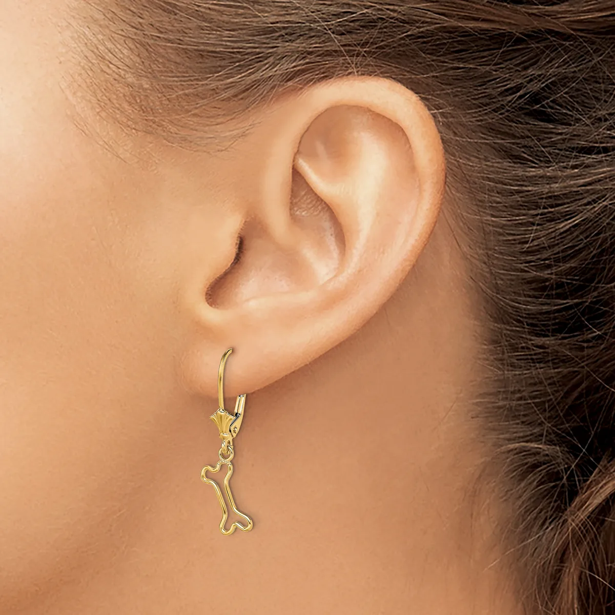 A person wearing a gold-toned dangle earring shaped like a bone, shown from the side view of their ear.