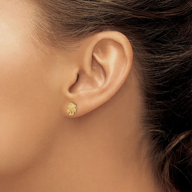 Close-up side view of a person's ear wearing a small textured gold stud earring in the earlobe.