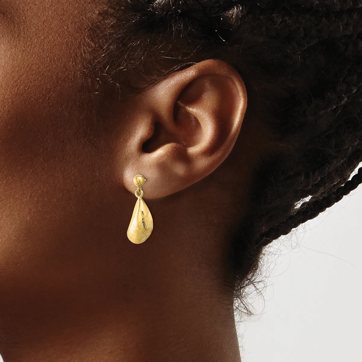 A woman wearing a gold teardrop earring with a textured finish, shown from the side view of her ear and neck.
