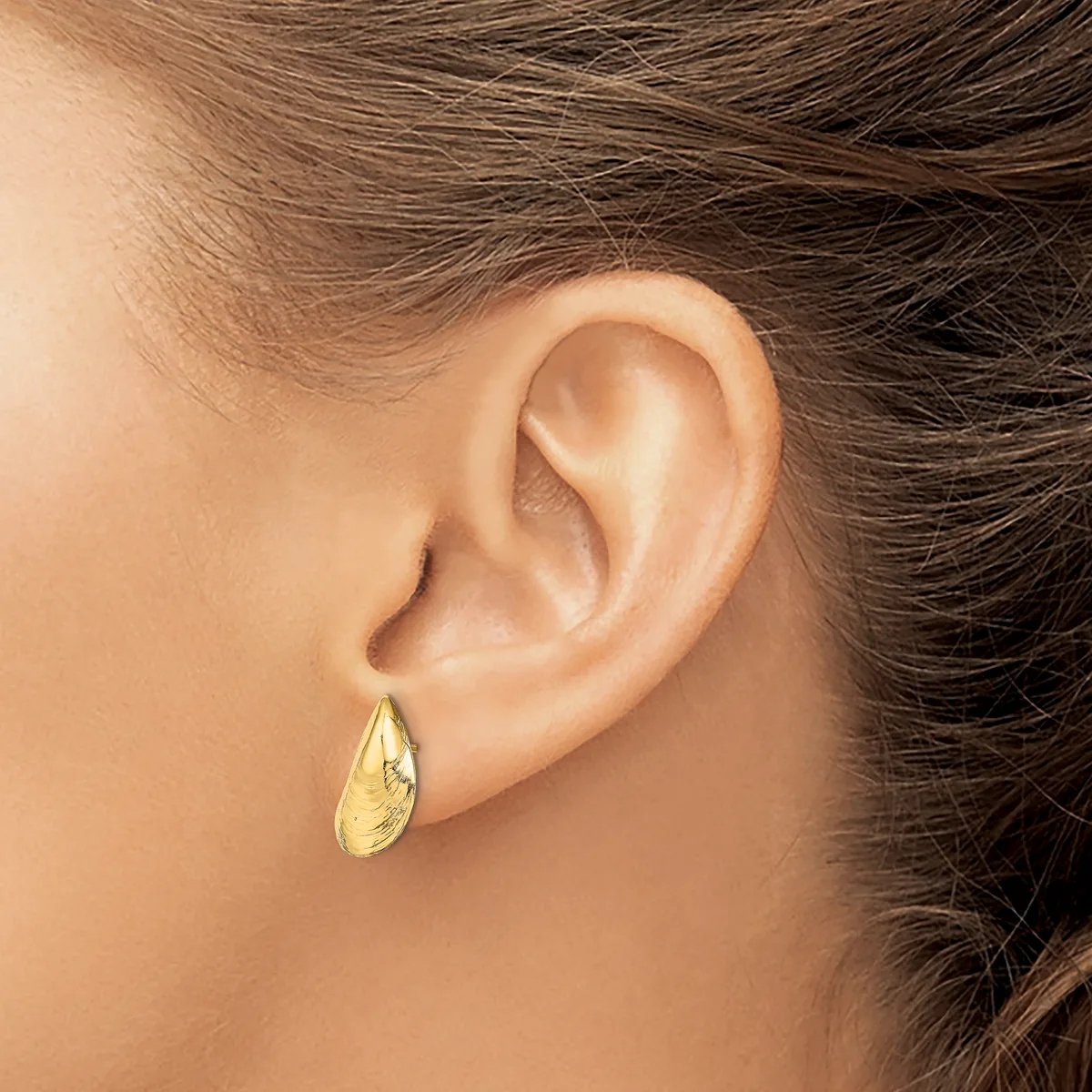 A person wearing a gold teardrop-shaped earring with a textured surface, shown from the side profile of their ear.