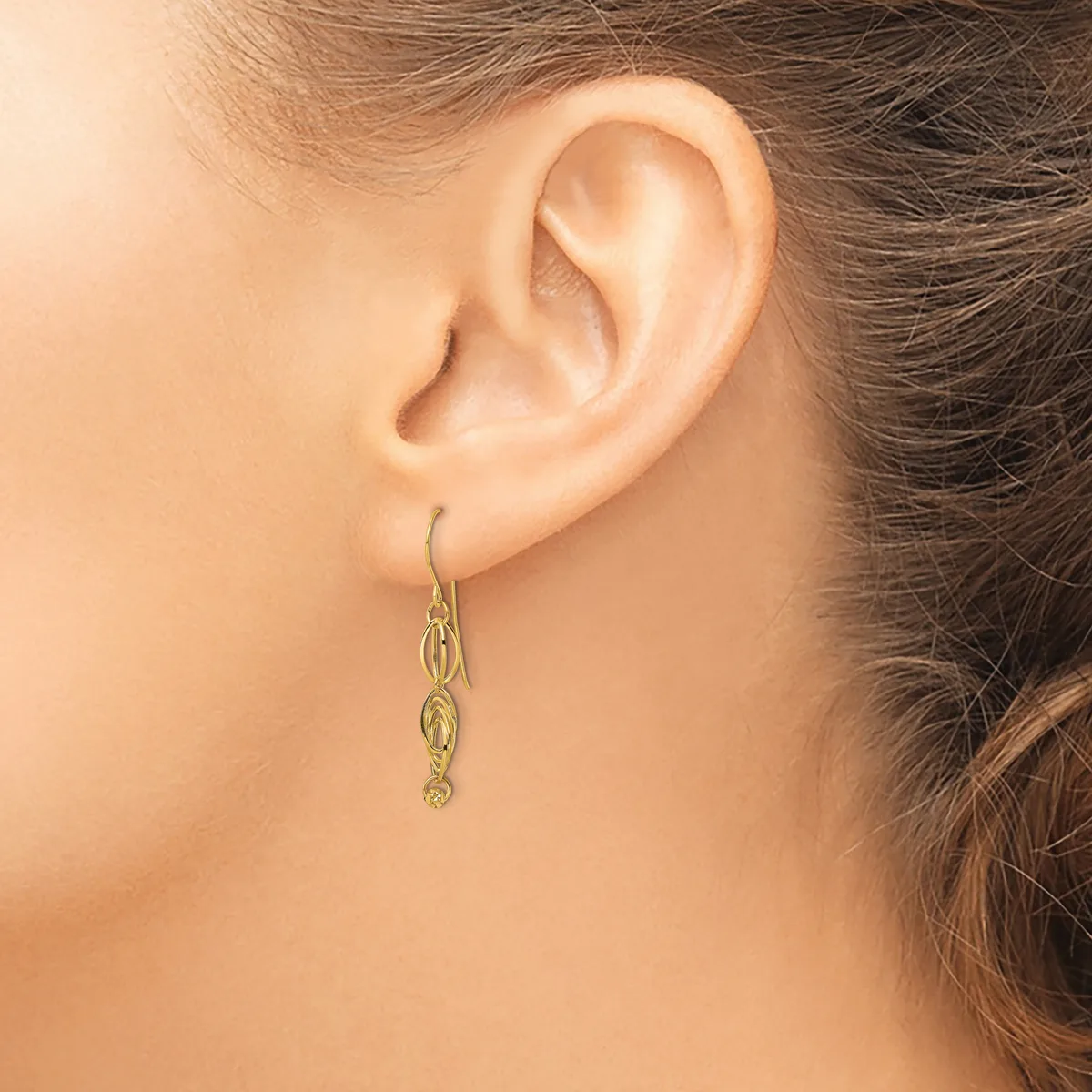 A person wearing a gold-toned dangle earring with oval link details, shown from the side view against their ear.