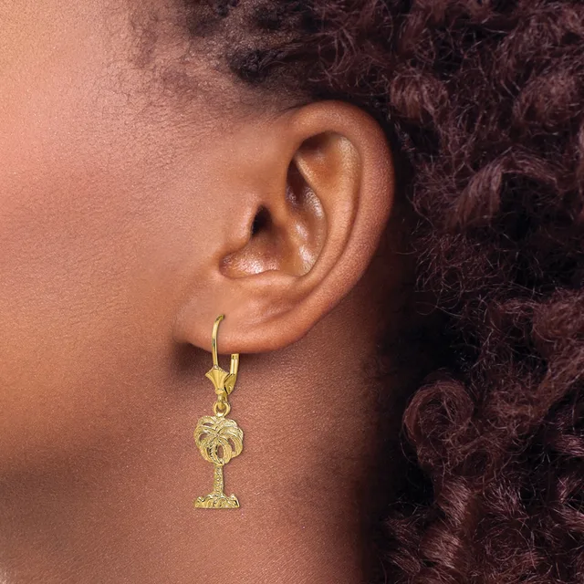 A person wearing a gold lever-back earring with a palm tree charm pendant hanging from it.