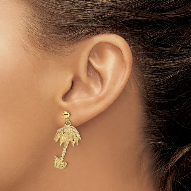 Gold palm tree dangle earrings with a small round post on a person's ear.