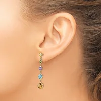A woman wearing a dangling earring with five colorful gemstones in gold settings, displayed on her earlobe against her neck and shoulder.