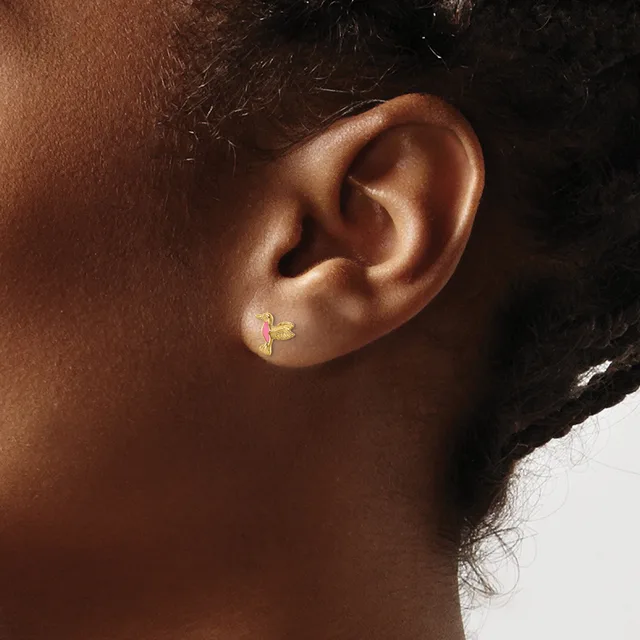 A small gold cross earring with a textured finish worn in the earlobe of a person shown in profile.