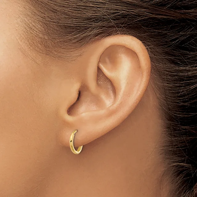 A person wearing a small gold curved hoop earring in their pierced earlobe, shown in profile against their bare shoulder and neck.