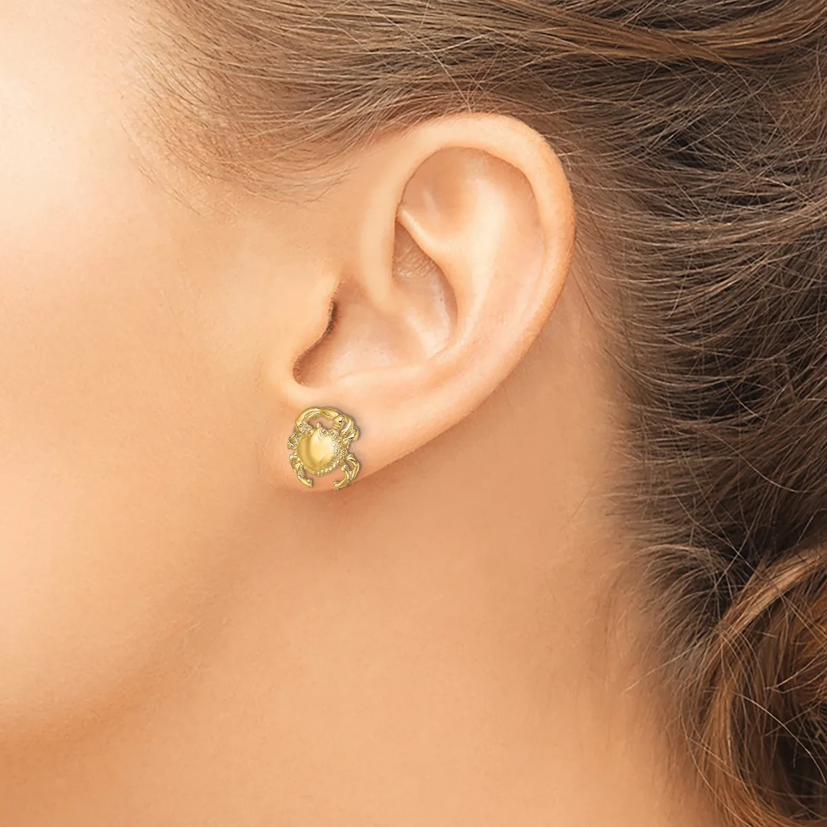 A person wearing a small gold stud earring with a pale yellow or citrine stone set in an ornate circular bezel, shown from the side view near the ear.