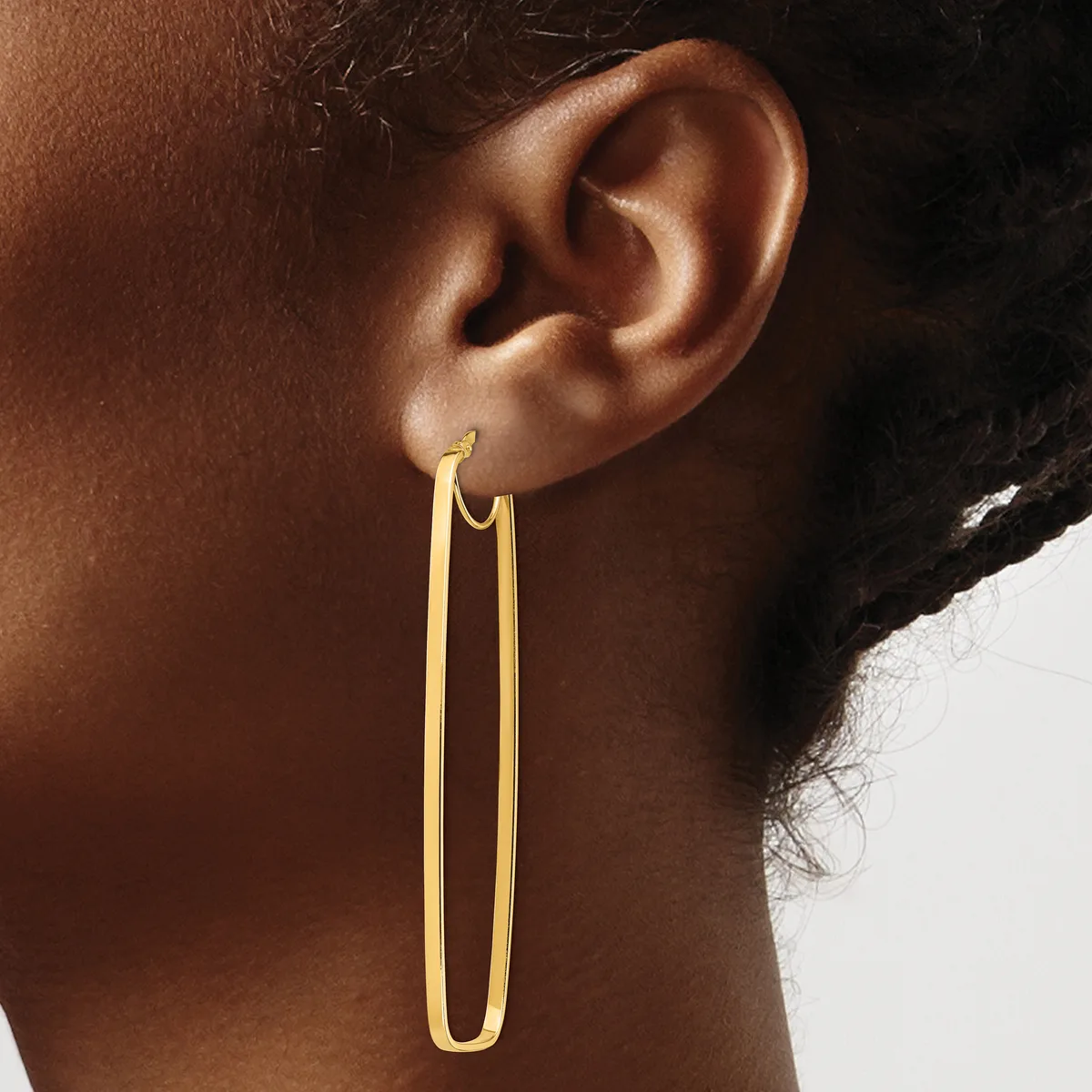 A person wearing a long, thin gold-colored oval hoop earring that extends down the side of their neck.