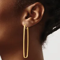 A person wearing a long, thin gold-colored oval hoop earring that extends down the side of their neck.