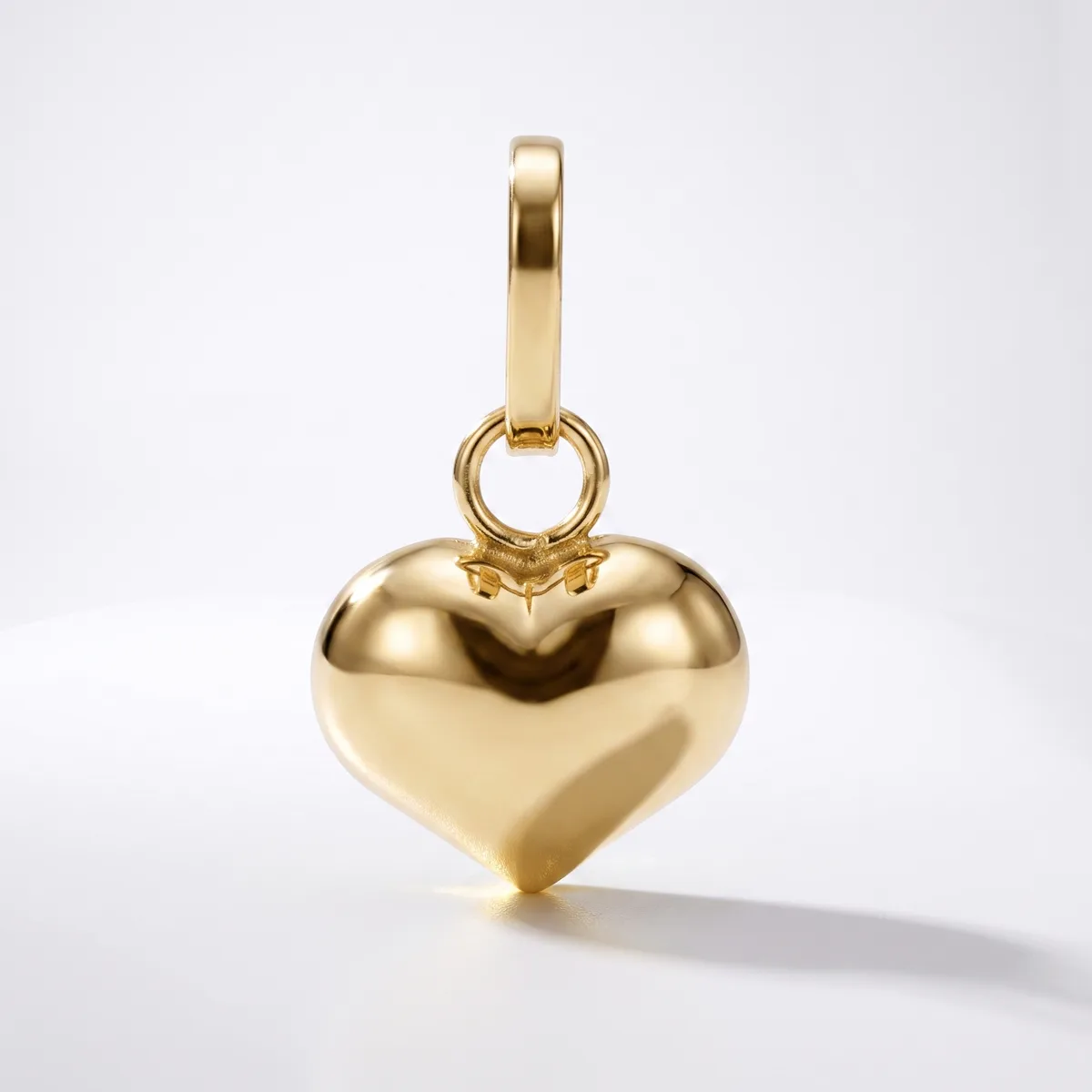 A polished gold heart-shaped pendant with a bail loop attached to the top, displayed against a white background.