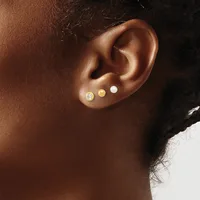Close-up side view of an ear with three small stud earrings in varying finishes: a sparkly stone, a gold disc, and a white pearl.