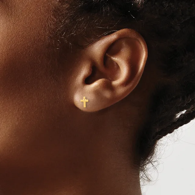 A person wearing a small gold cross earring in their earlobe, shown in profile against a neutral background.