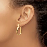 A woman wears a pair of polished gold hoop earrings with a smooth, rounded oval shape on her pierced ears.