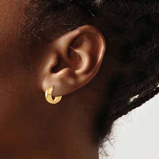 Close-up side view of a person's ear wearing a small curved gold hoop earring.