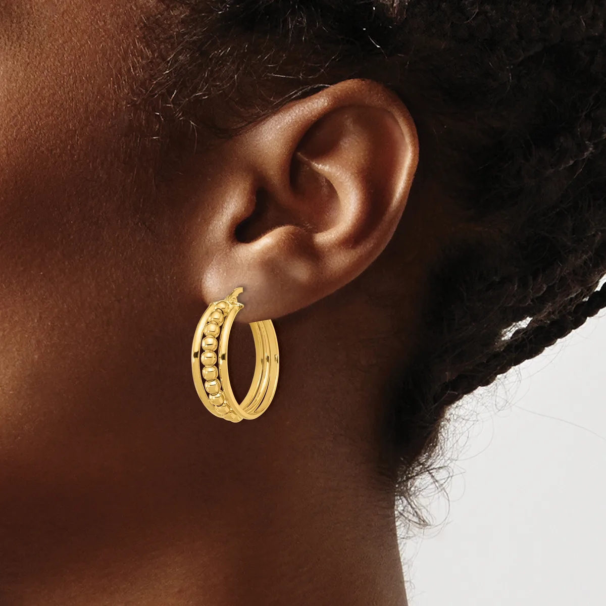 Gold hoop earrings with textured detailing on one side worn by a person shown in profile against a neutral background.