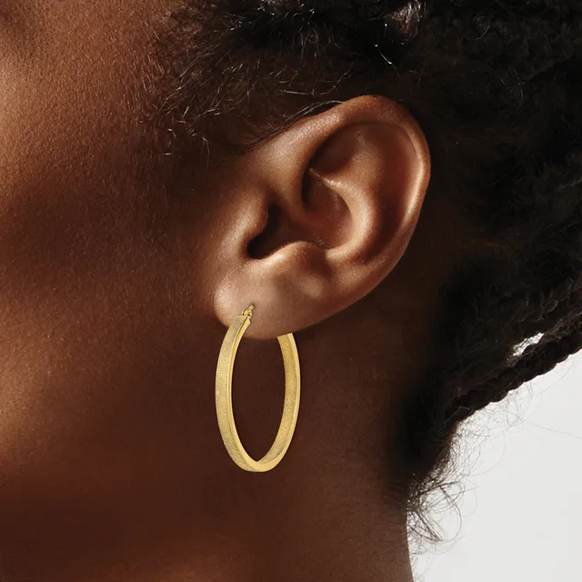 A person wearing a gold oval hoop earring, shown in profile with their ear and side of face visible against a neutral background.