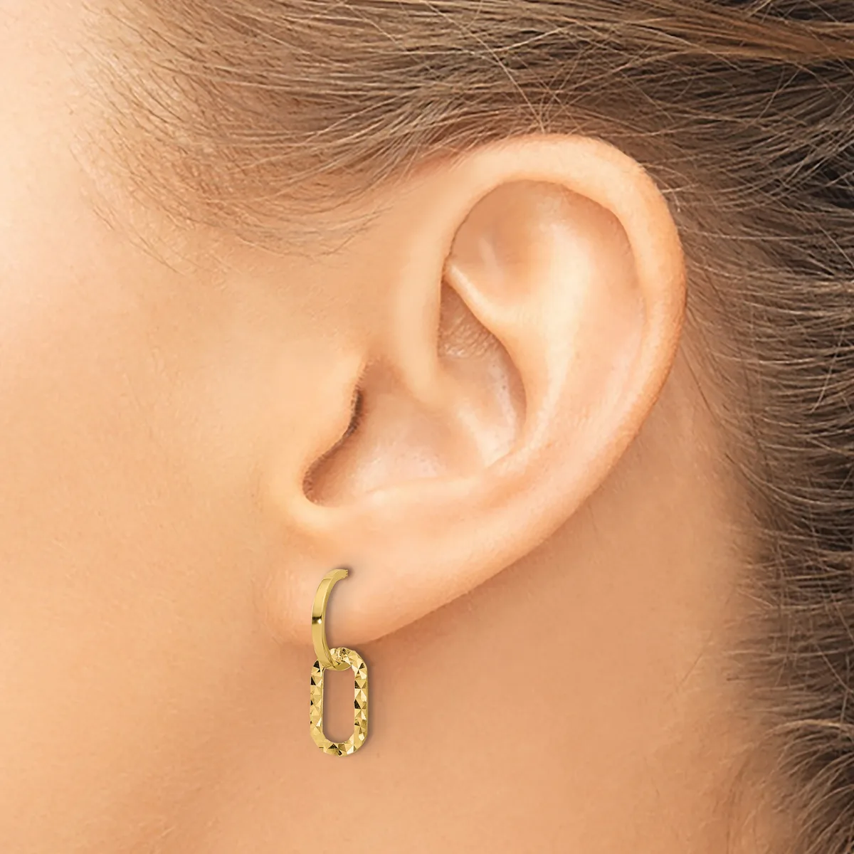 A close-up side view of a person's ear wearing a small gold textured oval hoop earring.