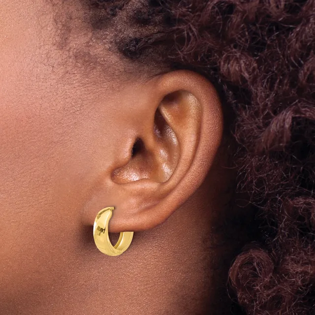 A close-up side view of a person's ear wearing a polished gold curved hoop earring.