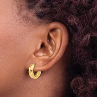A close-up side view of a person's ear wearing a polished gold curved hoop earring.