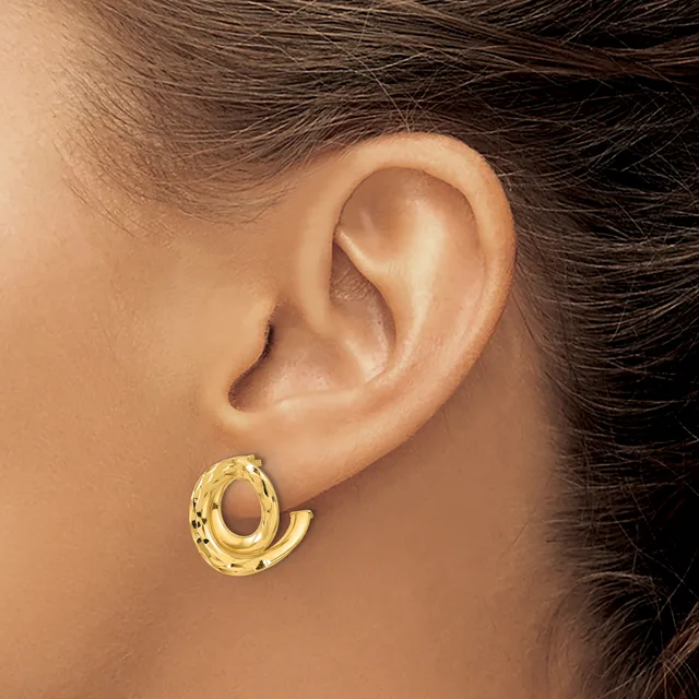 A woman wearing a textured gold-toned hoop earring with an open oval shape, shown from the side against her ear.