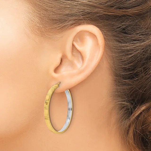 A close-up view of a person's ear wearing two oval hoop earrings, one with a textured gold finish and one with a smooth silver finish.