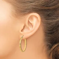 A person wearing a pair of gold-toned hoop earrings with a hammered texture, shown from the side profile of their ear.