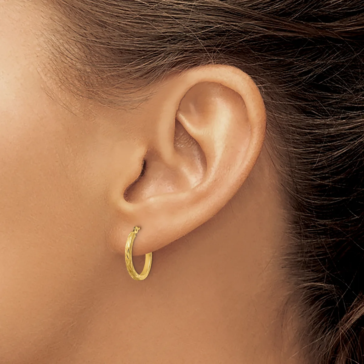 A gold hoop earring worn on the earlobe of a person shown in profile, with dark hair pulled back.