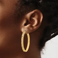 A person wearing a large gold hoop earring with a textured surface, shown in profile against a white and dark background.