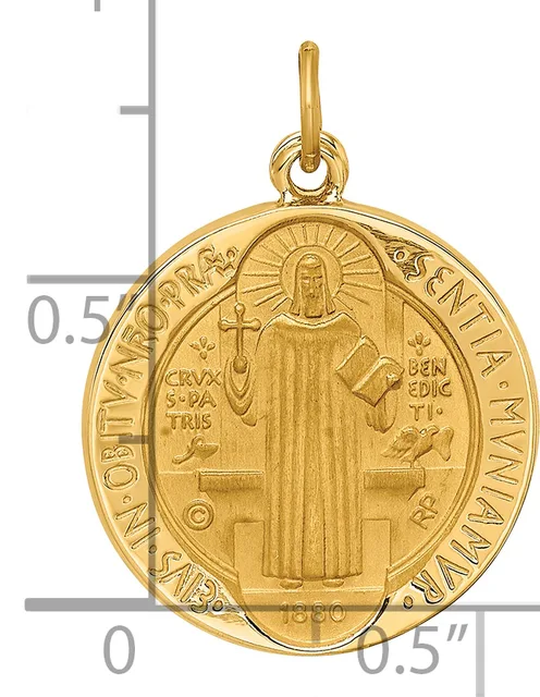Gold-toned religious medal pendant featuring Saint Benedict in robes holding a cross and book, surrounded by text on an oval frame with a bail loop at top, shown next to a measurement scale.