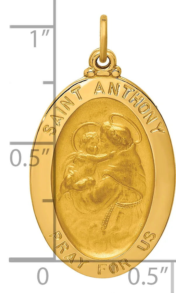 Gold oval pendant depicting Saint Anthony holding a child, with text around the border and a small loop at the top for hanging, shown next to a ruler for scale.