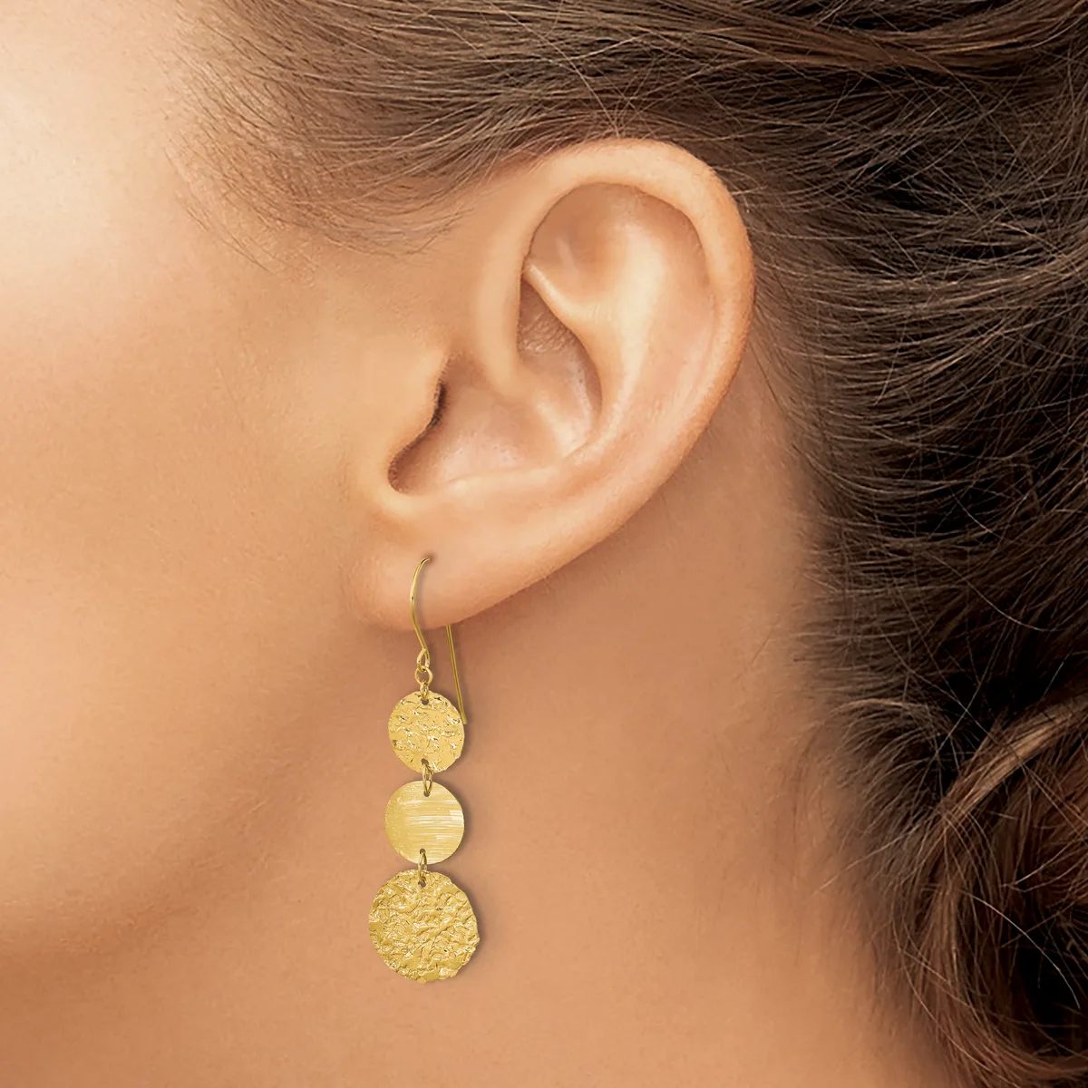 A woman wearing three-tiered gold disc drop earrings with textured and polished finishes hanging from her earlobe.