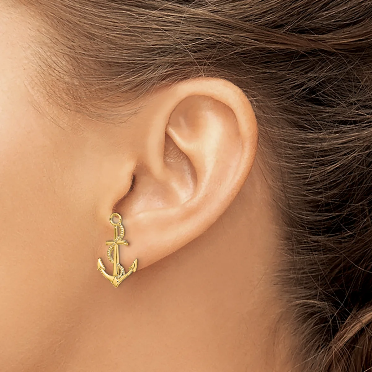 A gold anchor-shaped earring hanging from a person's earlobe, shown from the side view.