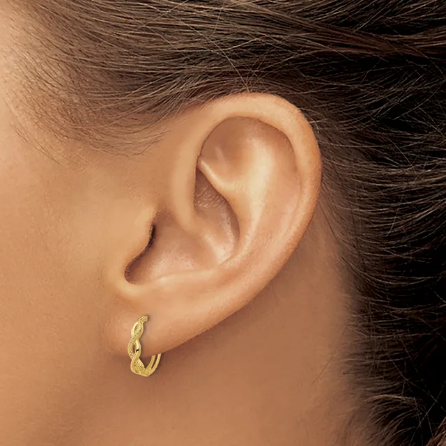 A person wearing a small textured gold hoop earring in their earlobe, shown in profile against their ear and shoulder.