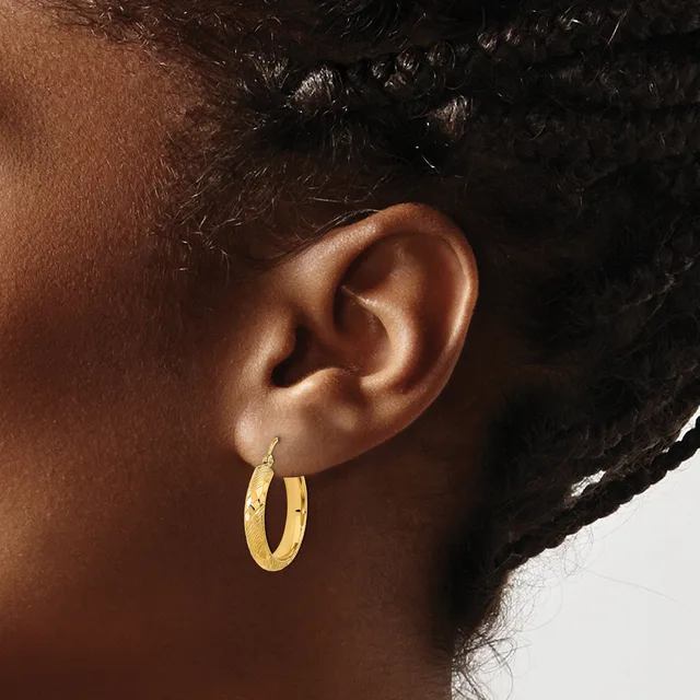Close-up side view of a person's ear wearing a pair of gold hoop earrings with a textured surface.
