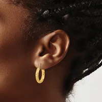 Close-up side view of a person's ear wearing a pair of gold hoop earrings with a textured surface.