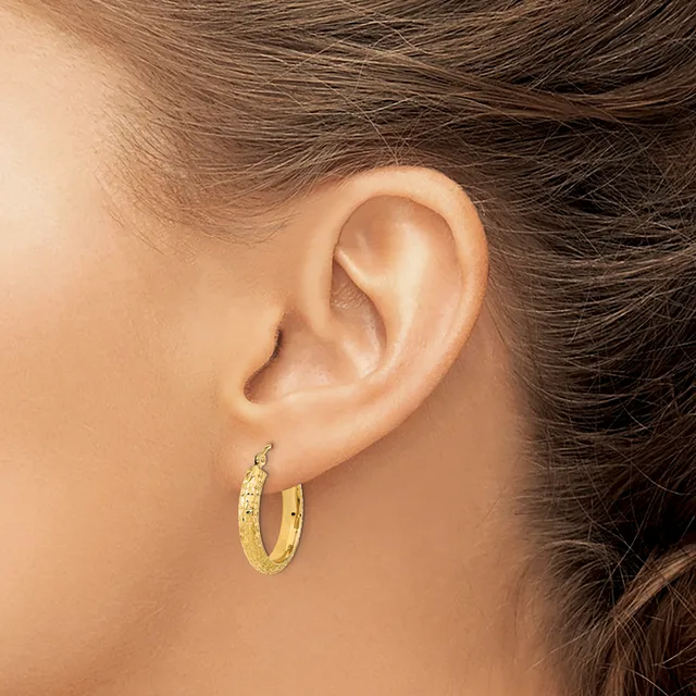 A person wearing a pair of textured gold hoop earrings with a hammered or dimpled finish, shown from the side view of their ear.