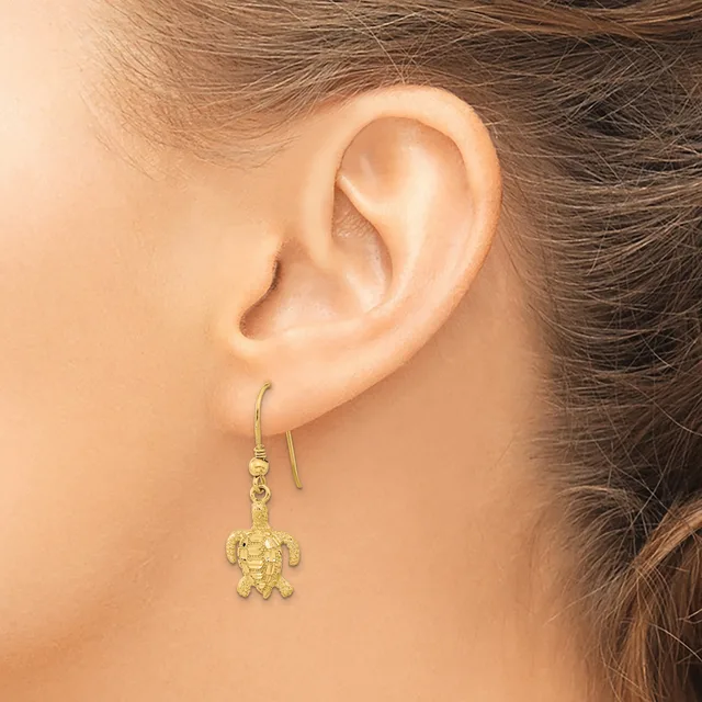 A woman wearing a gold turtle-shaped dangle earring on a hook, shown from the side view of her ear and neck.