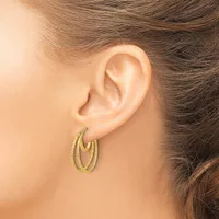 A woman wearing double oval hoop earrings with a textured finish in gold tone metal, shown from the side profile of her face and ear.