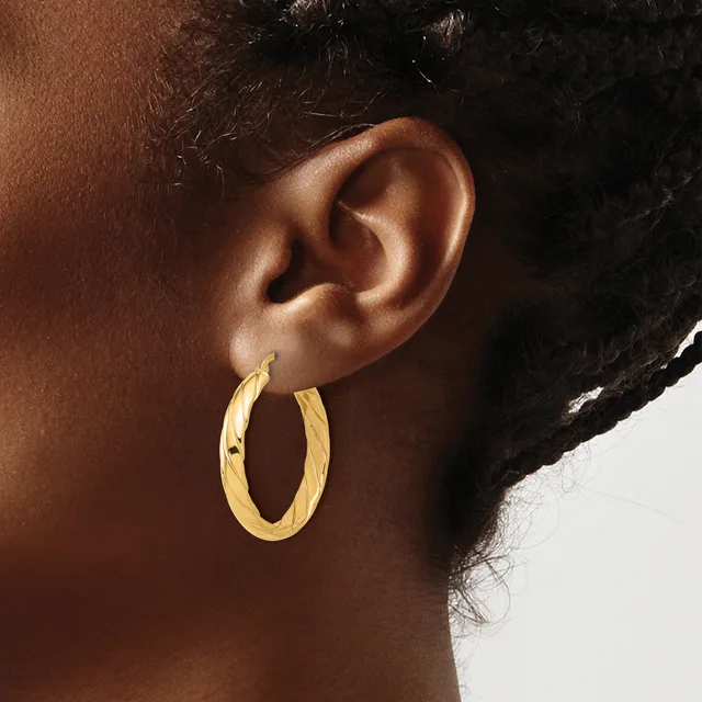 A person wearing a pair of gold hoop earrings with a twisted or textured surface, shown from the side view of their ear and neck.