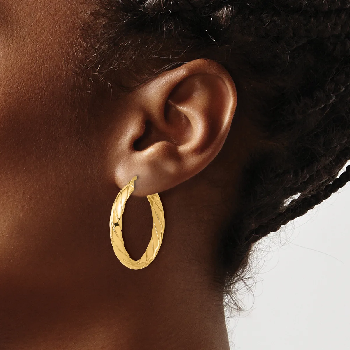 A person wearing a pair of gold hoop earrings with a twisted or textured surface, shown from the side view of their ear and neck.