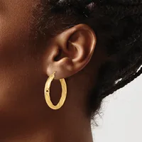 A person wearing a pair of gold hoop earrings with a twisted or textured surface, shown from the side view of their ear and neck.