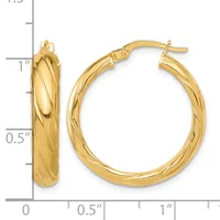 A pair of gold hoop earrings with a twisted textured surface, displayed next to a measurement ruler showing approximately one inch in length.