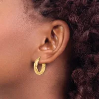A person wearing gold hoop earrings with a textured finish, shown in profile view against dark curly hair.