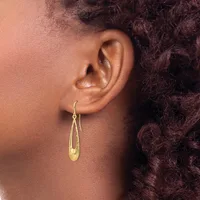 A person wearing a gold teardrop-shaped hoop earring with a textured surface, shown from the side profile against their ear.