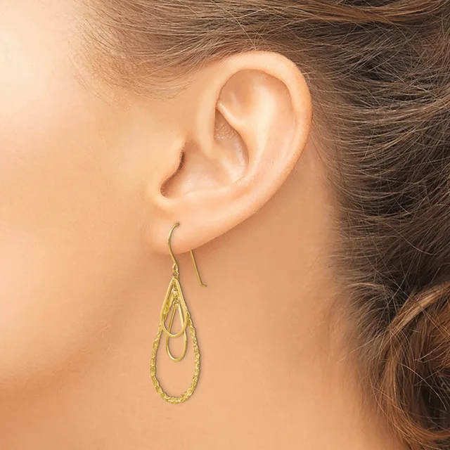A person wearing a pair of gold-colored teardrop-shaped dangle earrings with textured surfaces, shown from the side view of their ear and neck.
