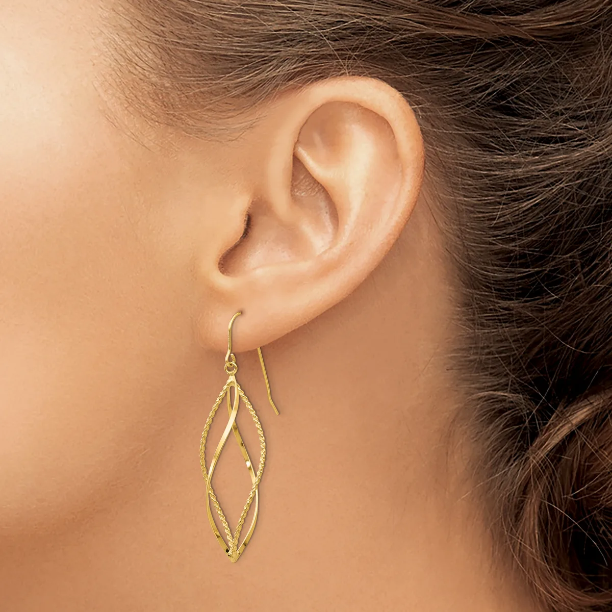 A woman wearing gold drop earrings with elongated diamond-shaped designs hangs from her earlobes.