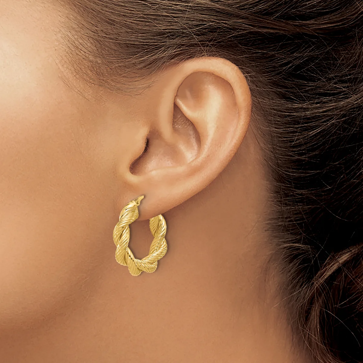A person wearing a pair of twisted gold hoop earrings with a textured finish, shown from the side profile of their ear and neck.