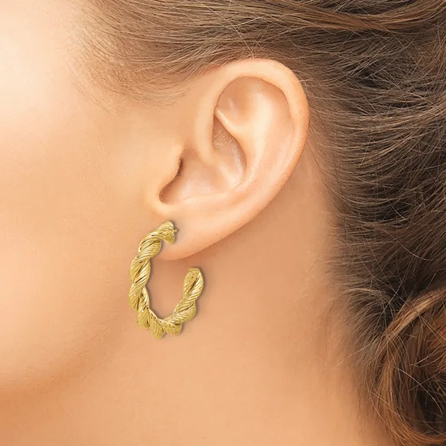 A person wearing a twisted textured gold hoop earring in their earlobe, shown in profile against their ear and brown hair.