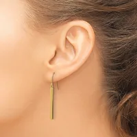 A person wearing a long, thin gold-colored drop earring on a fish hook ear wire, shown from the side view of their ear.