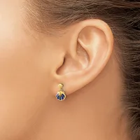 A woman wearing a small gold and blue enamel shell-shaped drop earring in her earlobe.